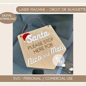 Puede incluir: Un letrero de madera con un gorro de Papá Noel rojo, texto blanco que dice "Santa Please Stop Here For Nico and Mati", y un colgador de cuerda marrón. El letrero está sobre un fondo marrón.
