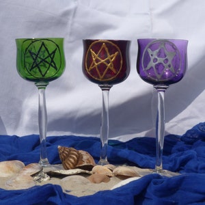 Könnte beinhalten: Drei Glaskelche mit unterschiedlich gefärbtem Glas und bemalten Pentagramm-Designs. Die Kelche sind grün, rot und lila.