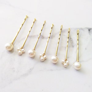May include: Set of seven gold hair clips with pearl accents. Some clips have a single pearl, while others have three pearls clustered together.