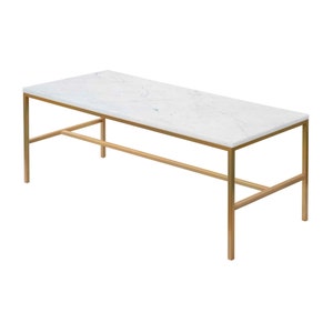 Op de afbeelding: Een rechthoekige salontafel met een wit marmeren blad en een gouden metalen frame.