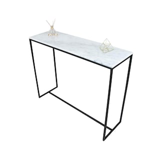 Peut inclure: Une console avec un plateau en marbre blanc et un cadre en métal noir. La table mesure 122 cm de long et 41 cm de large.