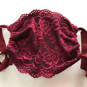May include: A burgundy lace face mask with adjustable ties. The mask is made of delicate lace with a floral pattern.