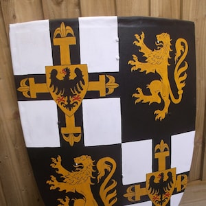 May include: A decorative shield with a black, white, and gold design. The shield features a checkered pattern with gold crosses and heraldic symbols, including eagles and lions. The shield is likely made of wood.