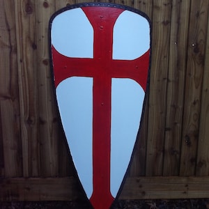 Könnte beinhalten: Ein weißer Schild mit einem roten Kreuz darauf bemalt. Der Schild ist aus Holz und hat einen Lederriemen.
