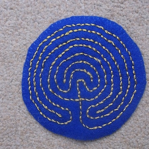 May include: A blue felt circle with a gold embroidered labyrinth design.