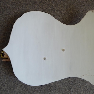 May include: A white, wooden wall decoration with a distinctive, curved form. It has a brass-coloured metal fitting and two small, silver-coloured studs. The item is painted white and has a slightly distressed look.