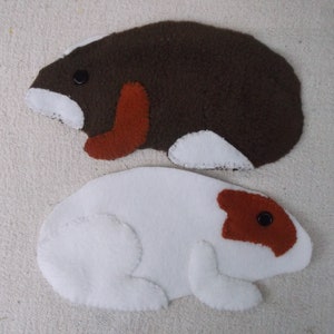 May include: Two felt animal shapes, one brown with white and orange accents, and one white with orange and black accents.