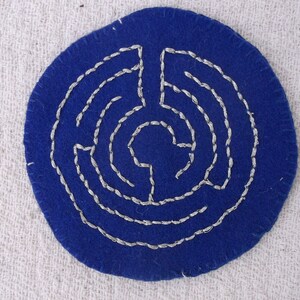 May include: A blue felt circle with a white embroidered labyrinth design.