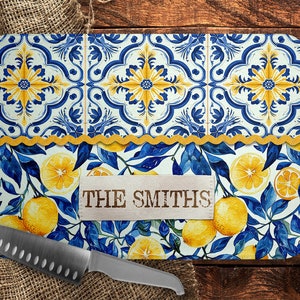 May include: A white cutting board with a blue and yellow tile pattern and a lemon motif. The board has a scalloped edge and a brown label with the text "THE SMITHS".