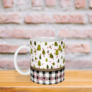 Può includere: Tazza in ceramica bianca con un motivo a albero di Natale e bacche rosse. La tazza ha una fascia a scacchi bianco e nero con un nastro di juta e il testo "Have a Cozy Christmas".