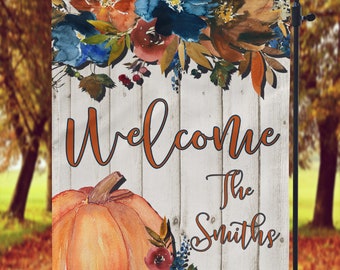 Può includere: Bandiera da giardino decorativa con un design ad acquerello di una zucca e composizioni floreali nei toni dell'arancione, blu e marrone. La bandiera recita "Welcome The Smiths" in un carattere corsivo su uno sfondo a venature di legno bianco.