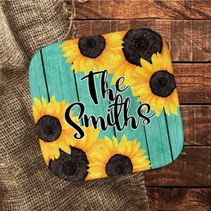 May include: A turquoise wooden sign with a distressed finish featuring a sunflower design and the text "The Smiths".