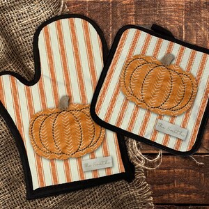 May include: Two orange and white striped kitchen pot holders with a stitched pumpkin design. The pot holders have black trim and the text "The Smiths" is printed on each.