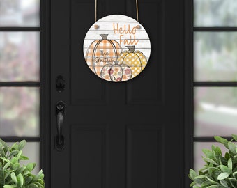 May include: A round wooden sign with a whitewashed background and the text "Hello Fall" in black. The sign features three pumpkins with orange, yellow, and white checkered patterns. The text "The Smiths" is written below the pumpkins.
