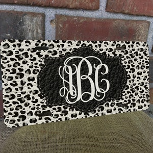 May include: A black and white leopard print license plate with a black leather-like monogram of the letters "HBC" in white.