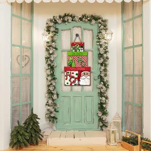 May include: A mint green door decorated for Christmas with a garland of white and green foliage. A stack of three decorative boxes hangs on the door, each with a different design and the words "The Smiths" and "Merry Christmas".