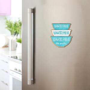 May include: Three turquoise and white decorative bowl magnets with a wooden border are stacked on a stainless steel refrigerator. The bowls have a vintage design and the text "the smiths" is printed on the bottom bowl.