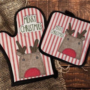 May include: A Christmas-themed oven mitt and pot holder set. The items feature a red and white striped pattern with a reindeer applique and the text "MERRY CHRISTMAS". The set is trimmed in black.