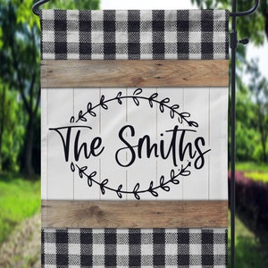 May include: Black and white checkered garden flag with a wooden sign that says "The Smiths" in a wreath of leaves.