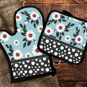 Puede incluir: Un juego de dos guantes de horno azul y blanco con un patrón floral y lunares negros. Los guantes están hechos de tela resistente al calor y son perfectos para proteger tus manos mientras cocinas.