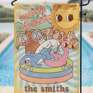 May include: A vintage-style garden flag with a retro sun, peace signs, and a whale and flamingo in a pool float. The text "Splish Splash" and "the smiths" is printed on the flag.