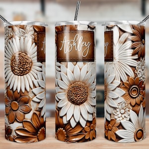 May include: Three stainless steel tumblers with a floral design. The tumblers are brown and white with a raised floral pattern. The middle tumbler has the name "Ashley" written on it.