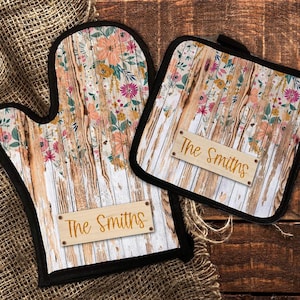 May include: A set of two oven mitts with a rustic woodgrain and floral design. The mitts have black trim and a personalized name tag that reads "The Smiths".