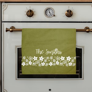 May include: A green kitchen towel with white floral border and the text "The Smiths" in white.