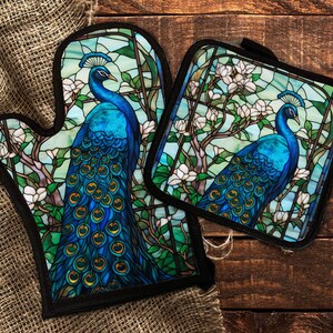 May include: A set of two oven mitts featuring a stained glass design of peacocks with blue, green, and gold accents. The peacocks are surrounded by white flowers and green leaves.