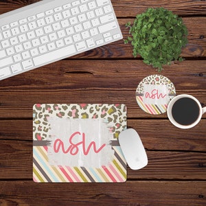 May include: A pink and gold mousepad with a leopard print and stripes. The mousepad has the name "ash" written in pink on it.