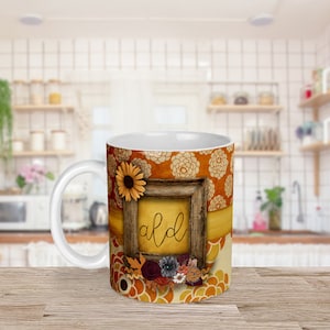 Può includere: Tazza in ceramica bianca con un design decorativo. La tazza presenta una cornice in legno con la parola "ald" in corsivo, un girasole e accenti floreali. Lo sfondo ha un motivo floreale nei toni dell'arancione e del giallo.