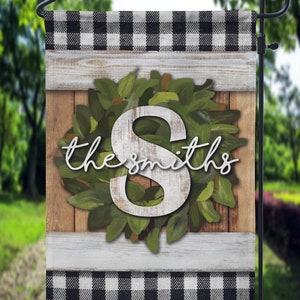 May include: A black and white checkered garden flag with a wooden background and a green wreath with the number 8 and the text "the smiths".