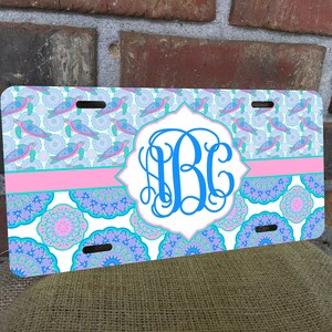 May include: A white personalized license plate with a blue, pink, and green sea turtle design. The plate has a pink stripe and a monogram in a blue circle.