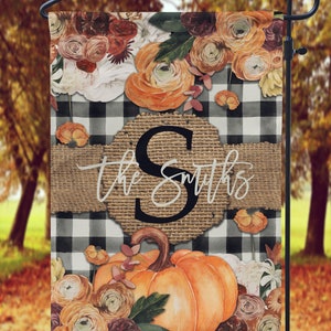 May include: A black and white checkered garden flag with a burlap banner that says "The Smiths" and a large orange pumpkin with fall flowers.