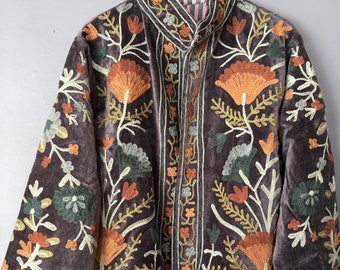 May include: A dark brown velvet jacket with detailed floral embroidery in orange, green, and cream. The jacket has a high collar and is buttoned. The embroidery features stylized flowers and leaves, creating an ornate design.