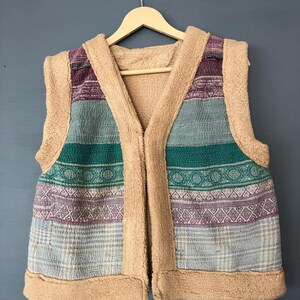 May include: A brown fleece vest with a multi-colored striped pattern. The vest has a V-neck and a zipper closure.
