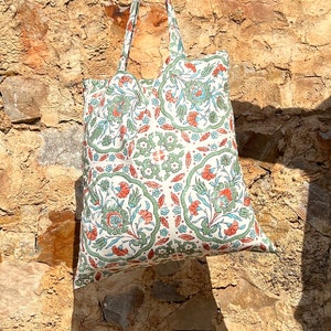 May include: A white tote bag with a green and orange floral pattern. The bag has two handles and is made of a lightweight fabric.