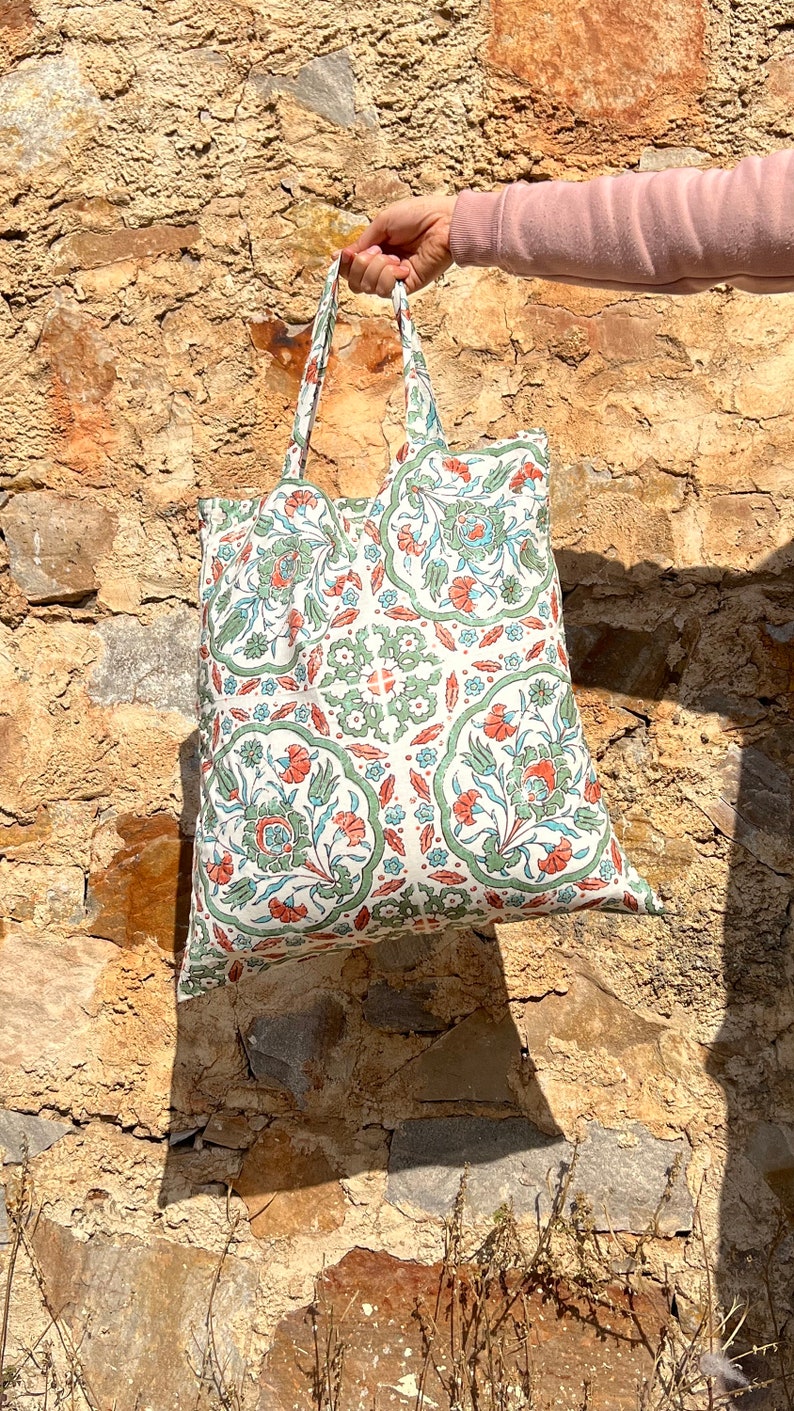 May include: A white tote bag with a green and orange floral pattern. The bag has two handles and is made of a lightweight fabric.