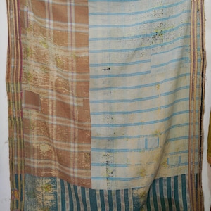 Puede incluir: Un textil rectangular grande con un diseño de patchwork. El textil presenta secciones de cuadros marrones, rayas azules y blancas y rayas verticales turquesas. Los bordes están adornados con un borde a rayas en tonos morados, amarillos y marrones.