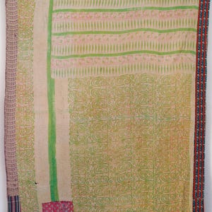 Può includere: Una trapunta vintage con un design patchwork. La trapunta presenta uno sfondo color crema con motivi verdi e rosa. I bordi sono rifiniti con un bordo a fantasia nei toni del rosso, blu e viola. Un piccolo quadrato rosa è cucito sulla trapunta.