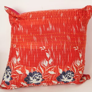 May include: Red and white floral patterned cushion with a pink backing and yellow stitching. The cushion is made of a soft, quilted fabric.