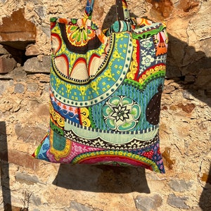 May include: A colorful tote bag with a paisley pattern in shades of blue, green, yellow, red, and pink. The bag has two black straps.