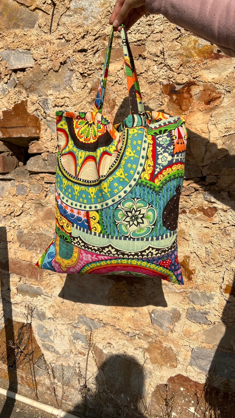 May include: A colorful tote bag with a paisley pattern in shades of blue, green, yellow, red, and pink. The bag has two black straps.