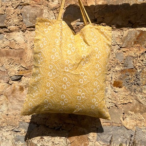 May include: A yellow tote bag with a white floral pattern. The bag has two handles and is made of a soft fabric.