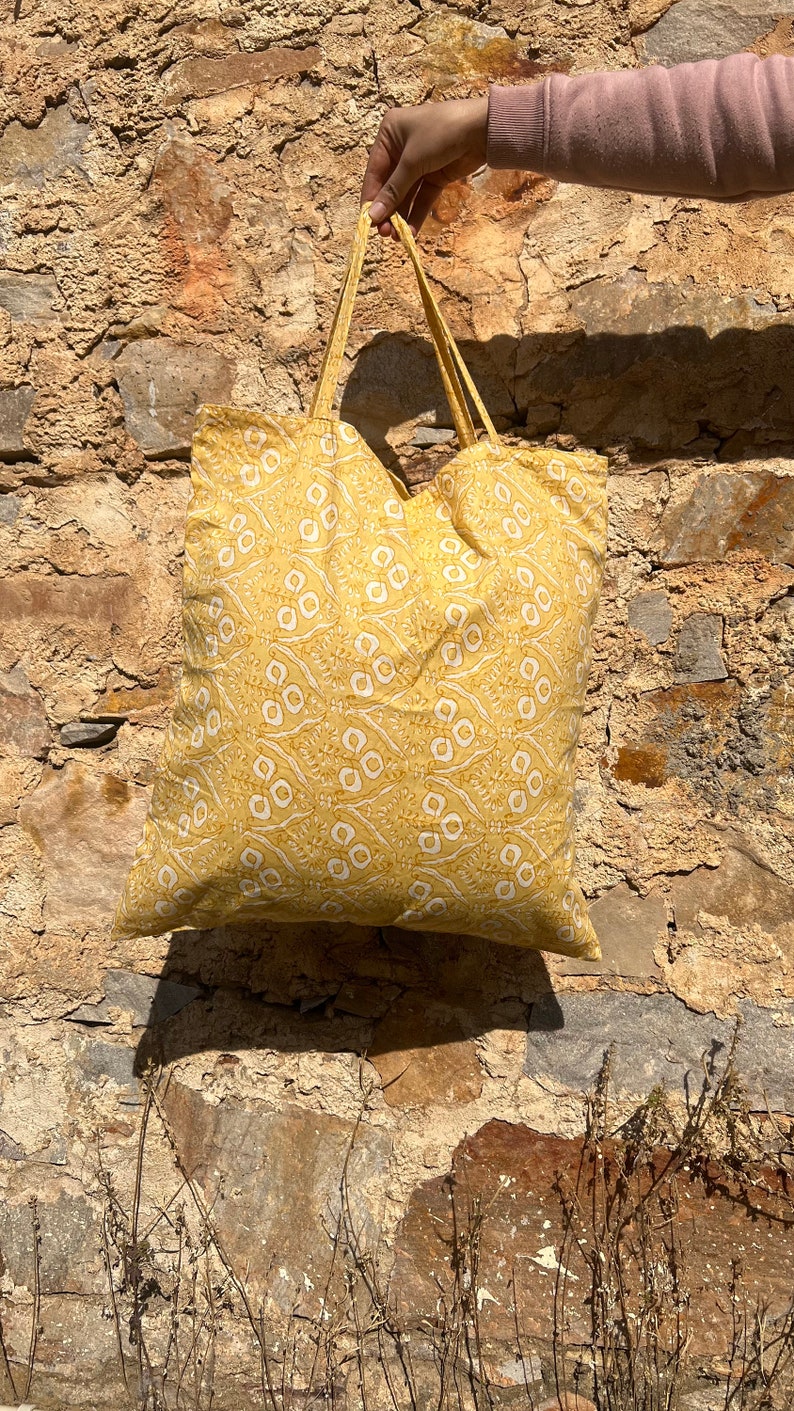 May include: A yellow tote bag with a white floral pattern. The bag has two handles and is made of a soft fabric.