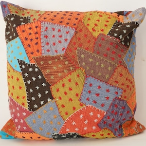 Könnte beinhalten: Ein Patchwork-Kissenbezug mit verschiedenen Farben und Texturen. Der Bezug besteht aus verschiedenen Stoffen, die in einem zufälligen Muster zusammengenäht sind. Der Stoff ist eine Mischung aus Braun, Orange, Blau und Rot.