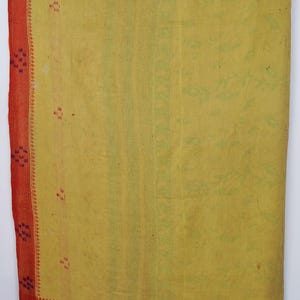 May include: A rectangular textile featuring a large central panel in a muted yellow hue, bordered by a contrasting red fabric. The surface is adorned with small, scattered geometric embroidery patterns in dark blue and red thread throughout.