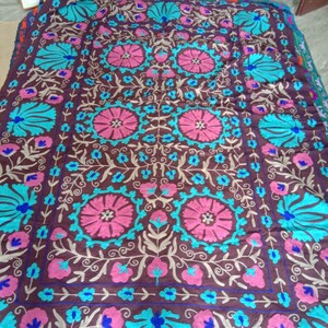 May include: A brown fabric throw blanket with a floral pattern embroidered in pink, blue, and white thread.