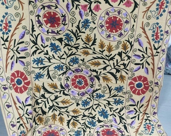 Pode incluir: Têxtil creme com um intrincado design floral. O padrão apresenta grandes flores vermelhas e roxas, detalhes azuis e rosa e folhagem verde escura. A borda tem um motivo floral e paisley repetido.