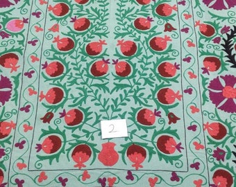 May include: A light blue fabric with a floral embroidery design. The design features a central motif of a tree with red and green pomegranates, surrounded by a border of pink and purple flowers. The fabric has a number "2" written on it.